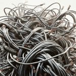 The image shows a chaotic tangle of numerous electrical cables. The cables are intertwined in a dense, disorganized mass, with many ends frayed and exposing copper wires. The overall scene conveys a sense of disorder and complexity, highlighting the intricate network of wires and their damaged insulation. This image represents the need for electrical service upgrades.